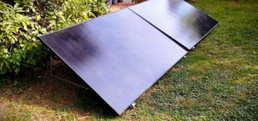 Two black solar panels positioned on a garden lawn near bushes, angled to capture sunlight.