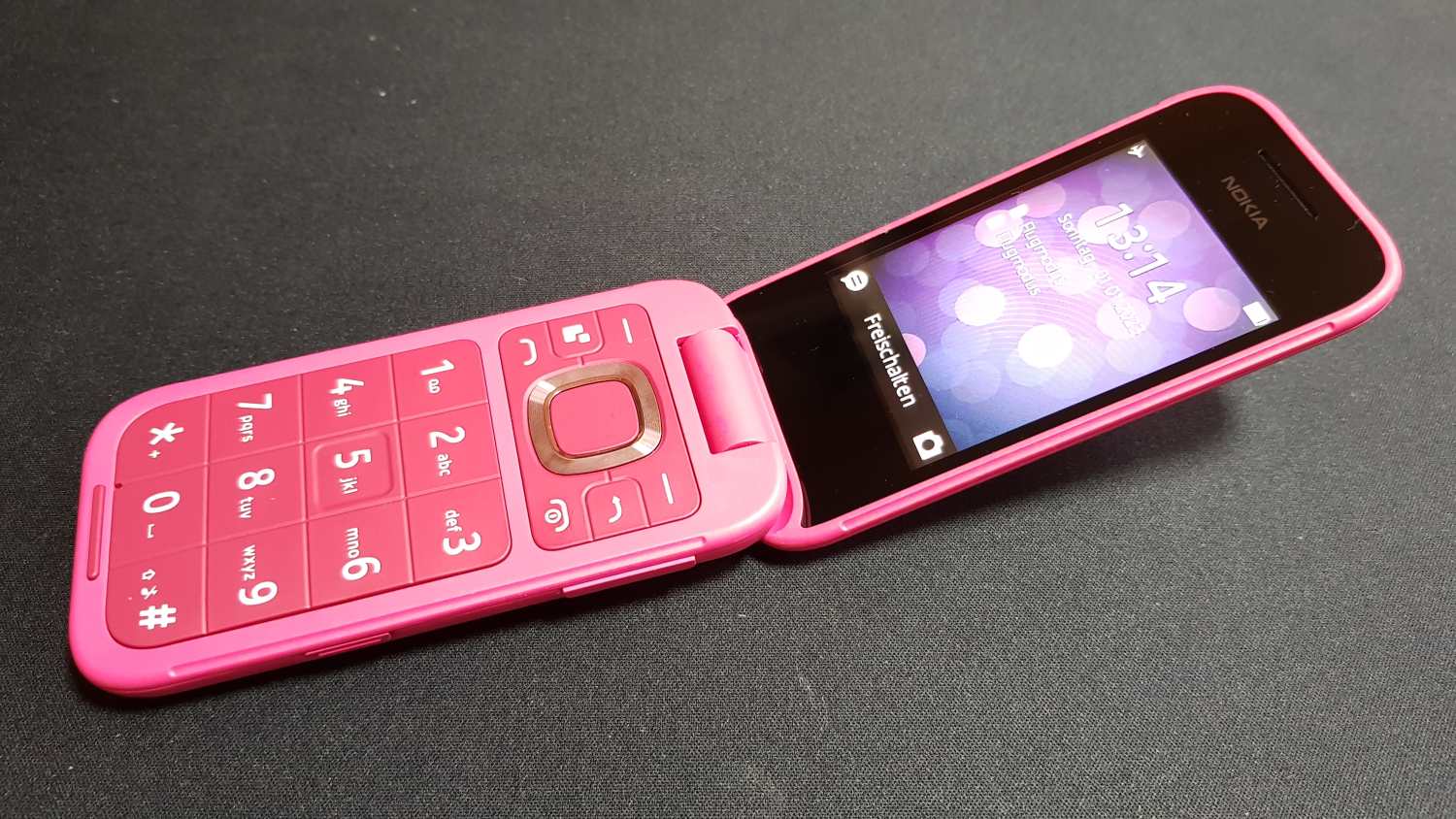 Pink Nokia 2660 Flip phone, partially opened, displaying home screen.