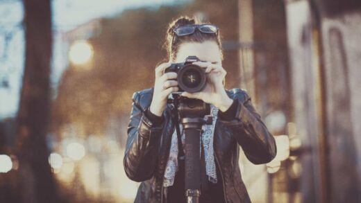 A woman holding a camera on a tripod, taking a photo outdoors.