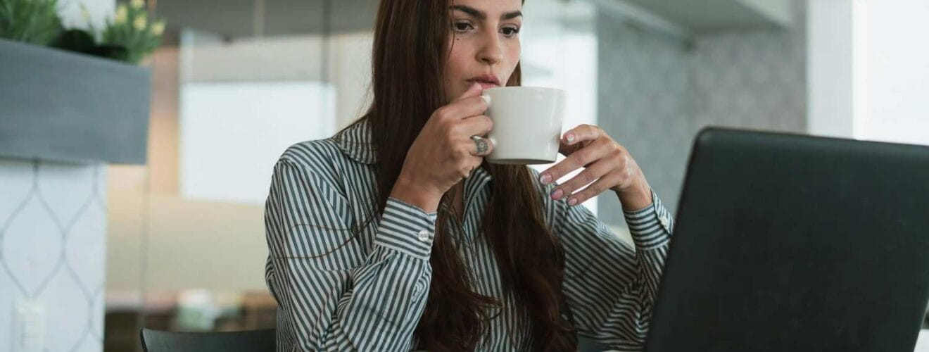 Woman drinking coffee while working on a laptop.