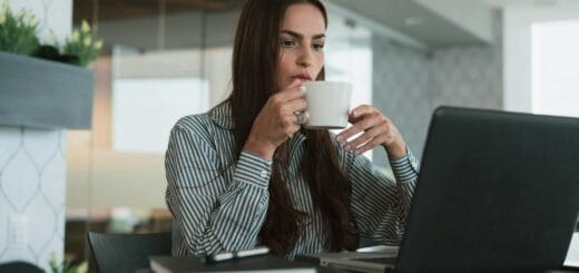 Woman drinking coffee while working on a laptop.