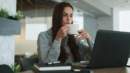 Woman drinking coffee while working on a laptop.